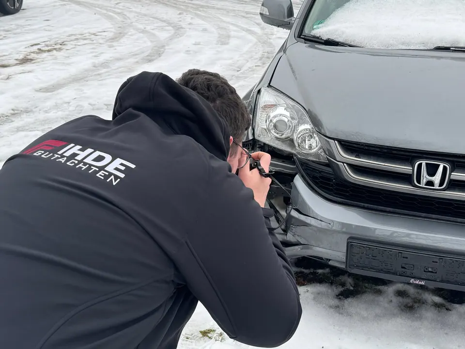 Sachverständiger dokumentiert Unfallschaden an Auto mit Kamera im Schnee
